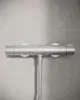 Thermostat von Ideal Standard, in silberner Ausführung, montiert an einer hellen Wand. Die Steuerungsventile sind seitlich angebracht.